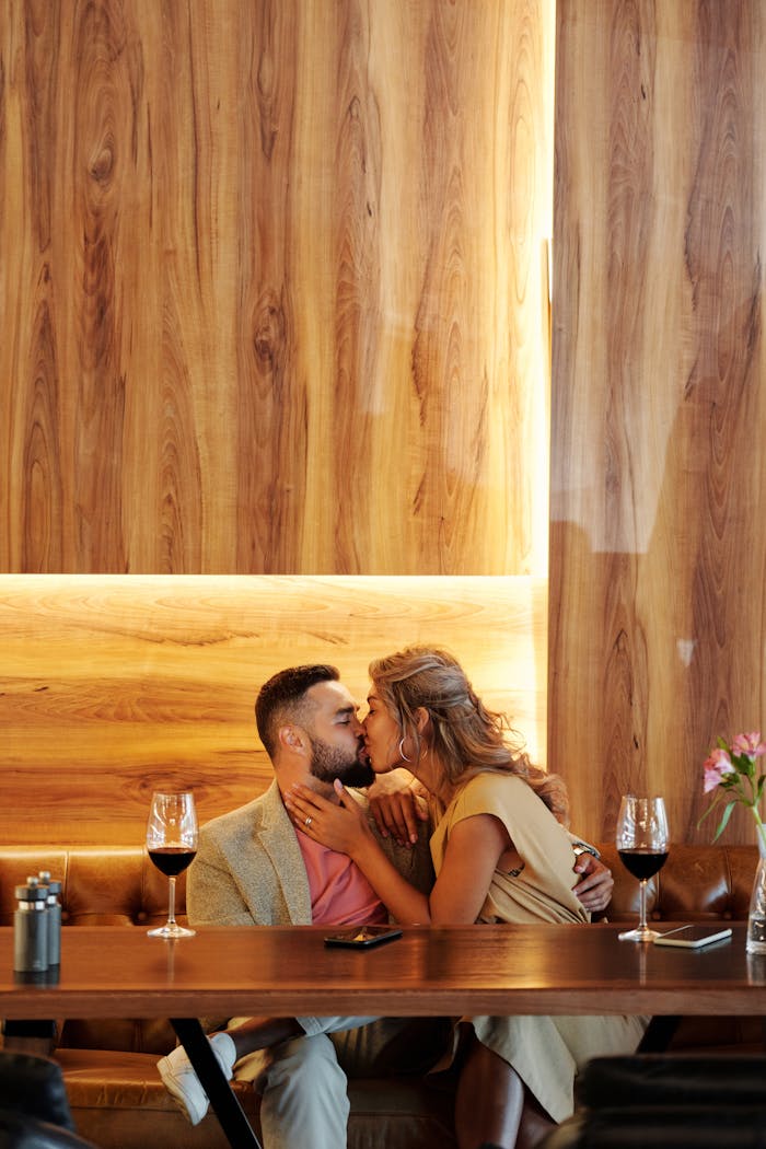 A romantic couple sharing a kiss over wine in a modern restaurant setting.
